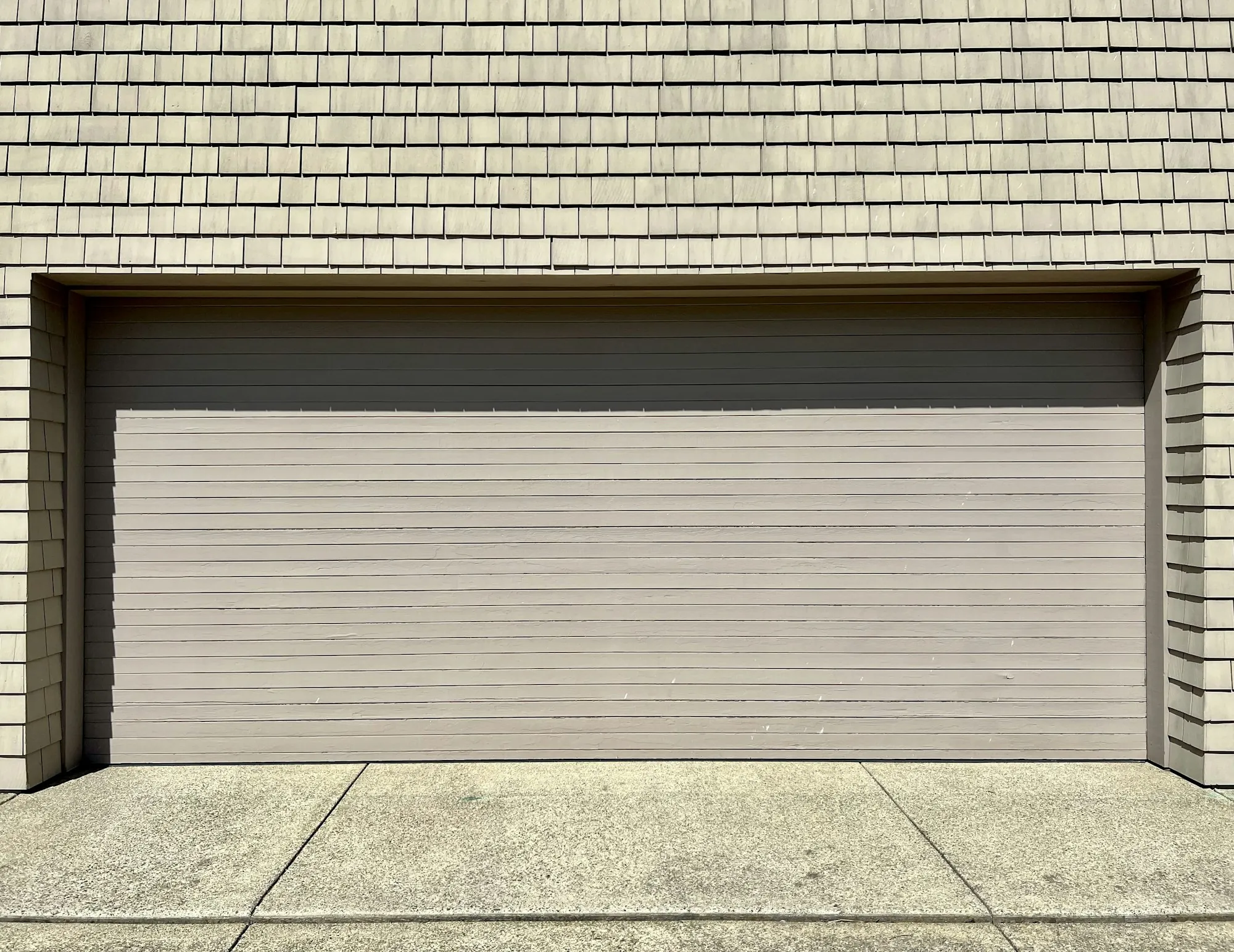 Wide closed garage door set into a shingle-sided wall